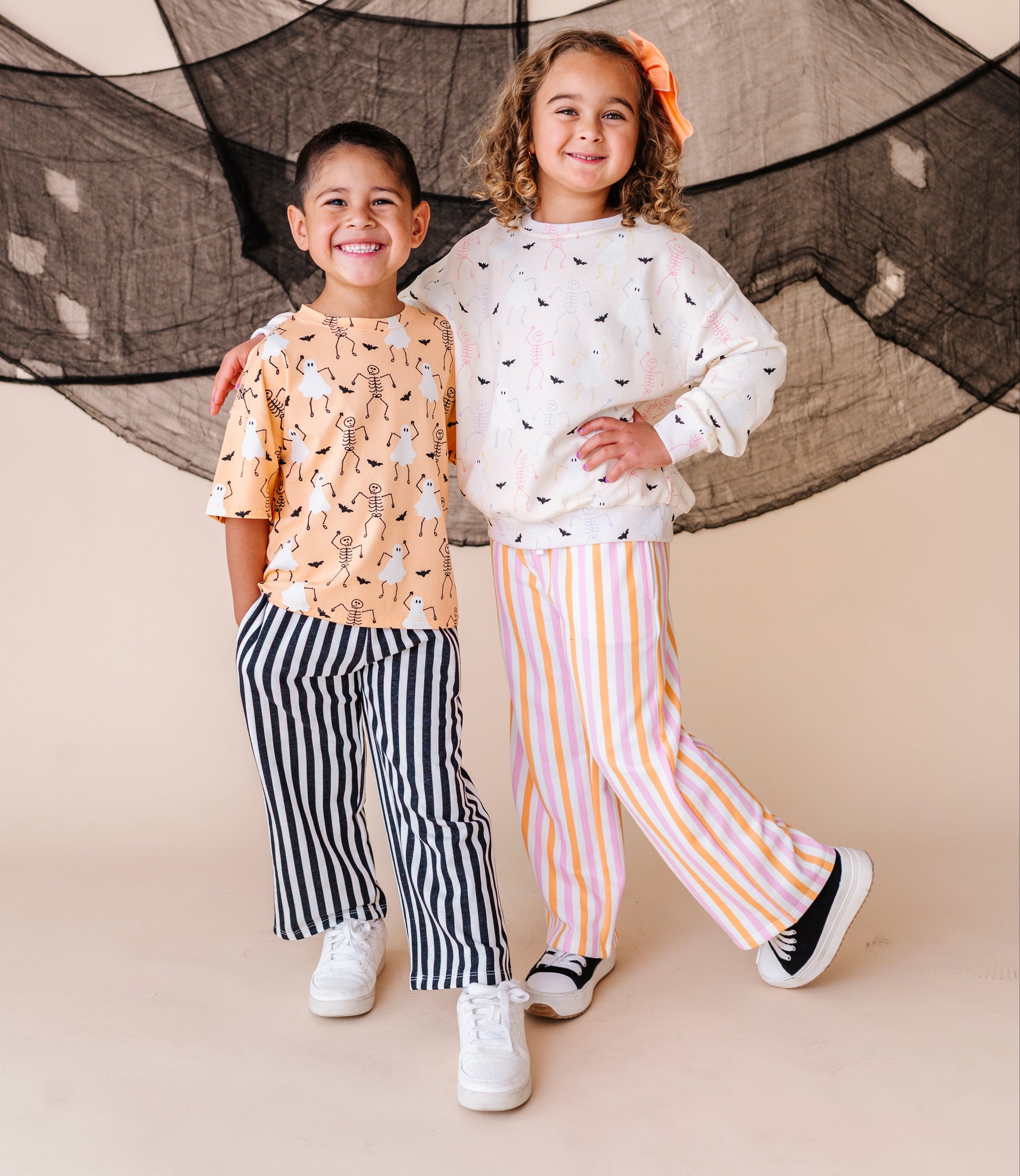 Two children standing together in front of a decorative net on a beige background