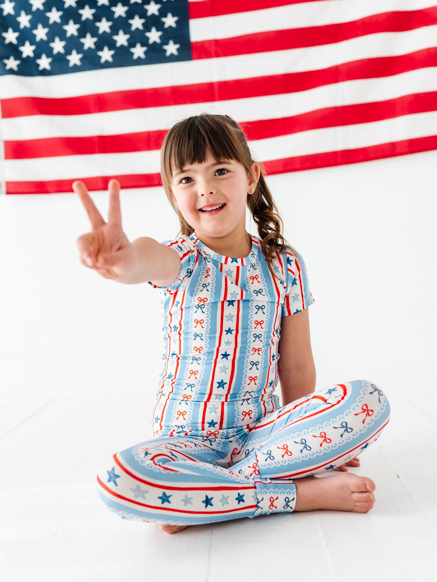 Child in a patriotic bamboo pajama outfit sitting on the floor with an American flag in the background