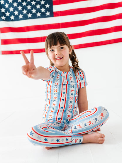 Child in a patriotic bamboo pajama outfit sitting on the floor with an American flag in the background