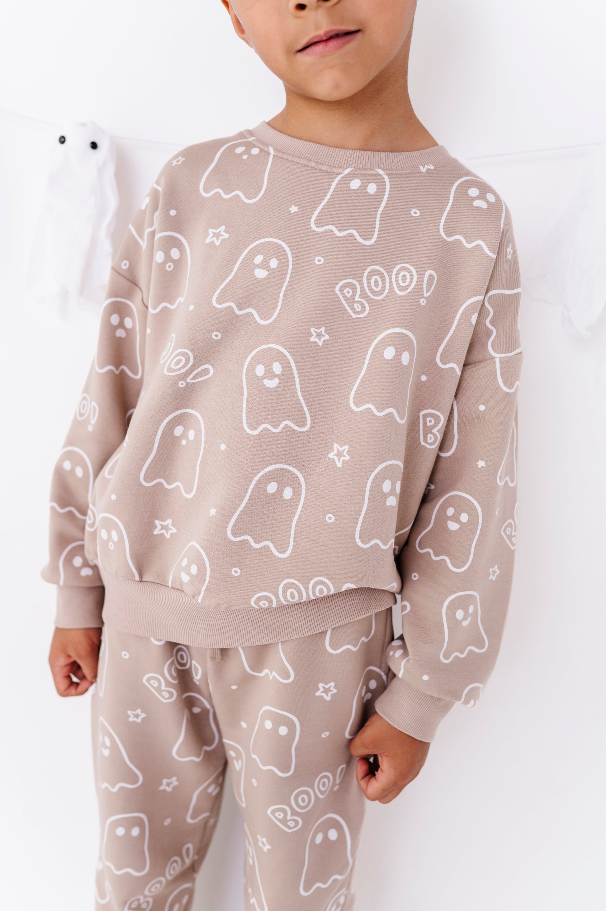 A child wearing a matching beige pajama set with a white ghost and star pattern, featuring a sweatshirt and pants.