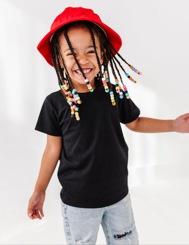 little girl dressed in a black t shirt and jeans wearing a red hat.