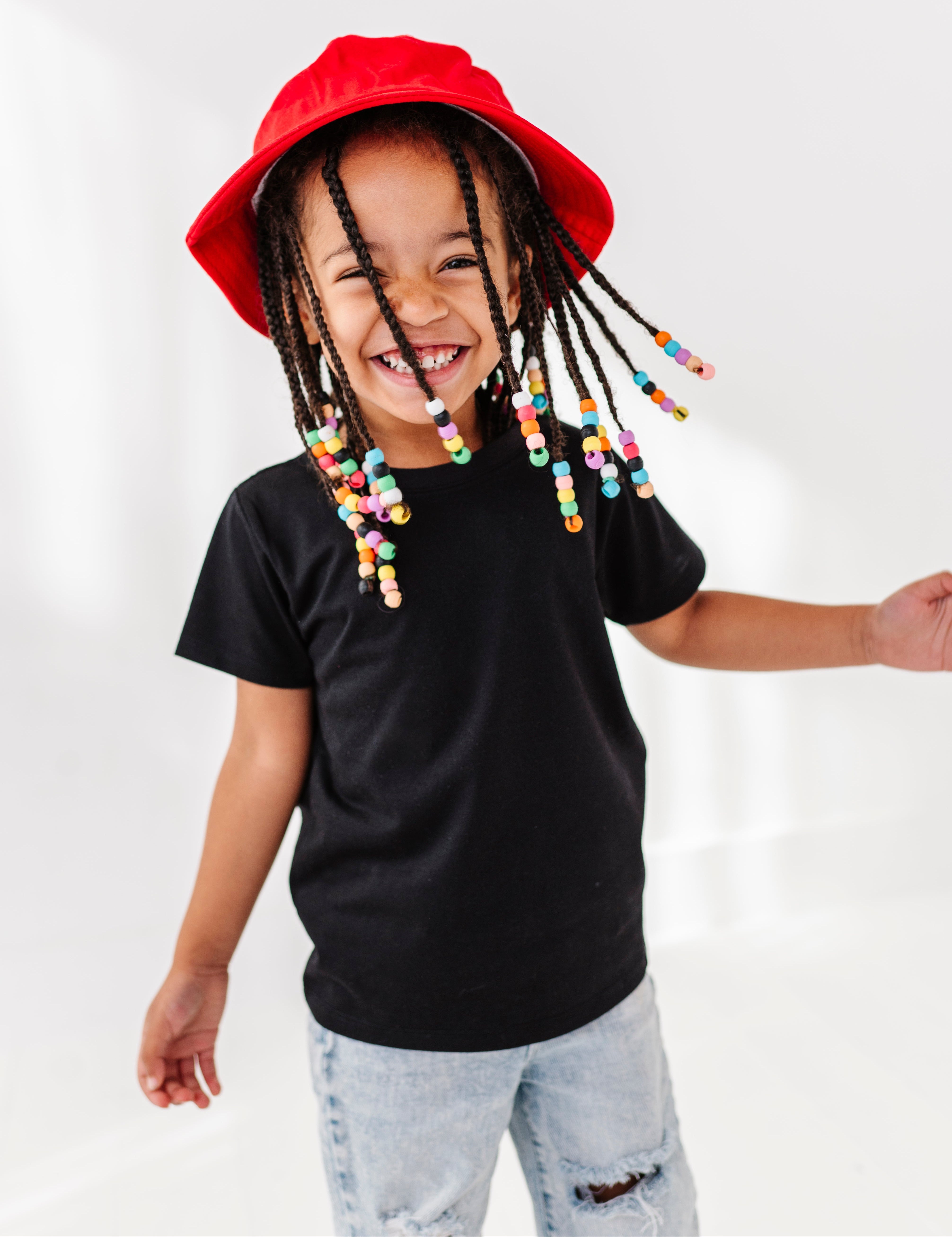 little girl dressed in a black t shirt and jeans wearing a red hat.