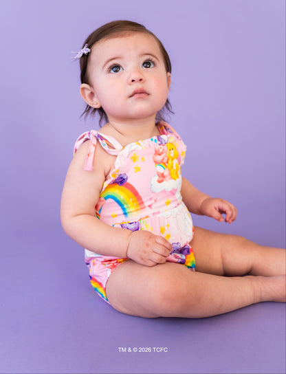 Baby wearing a colorful rainbow-themed Care Bears™ bamboo bubble romper against a purple background