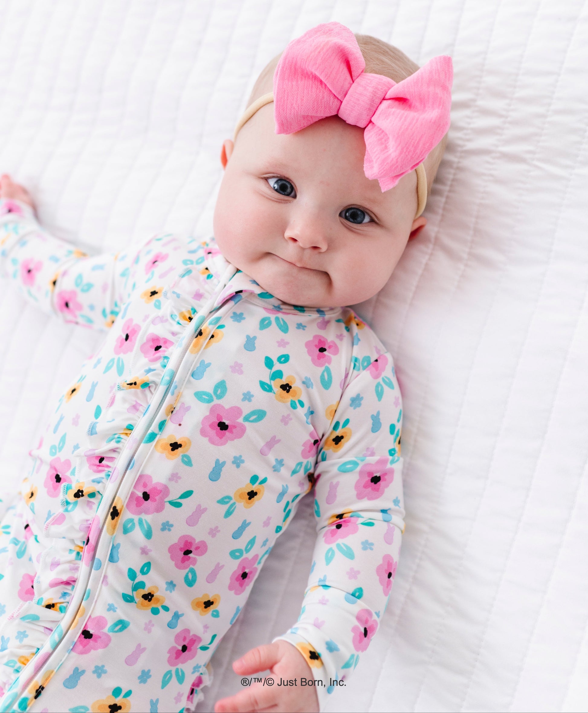 Baby wearing a floral bamboo romper and pink bow headband on a white background