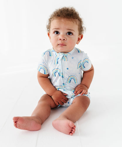 Baby wearing a white bamboo shortie romper with blue watercolor rainbow patterns on a white background