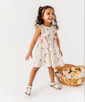 Young girl in a floral bamboo dress standing next to a basket of flowers on a white background