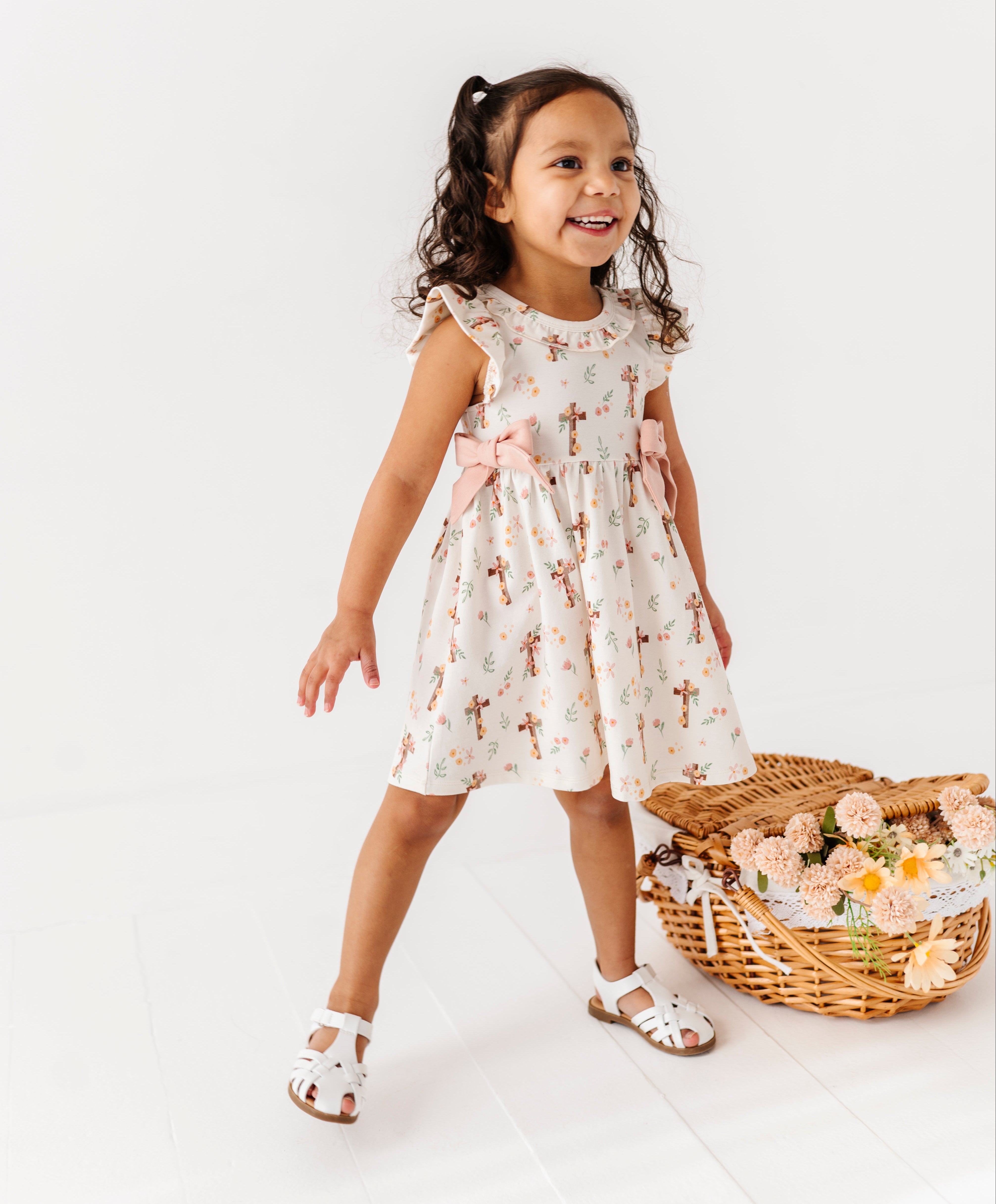 Young girl in a floral bamboo dress standing next to a basket of flowers on a white background