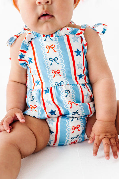 Baby wearing a patriotic bubble romper with straws and bows on a white background