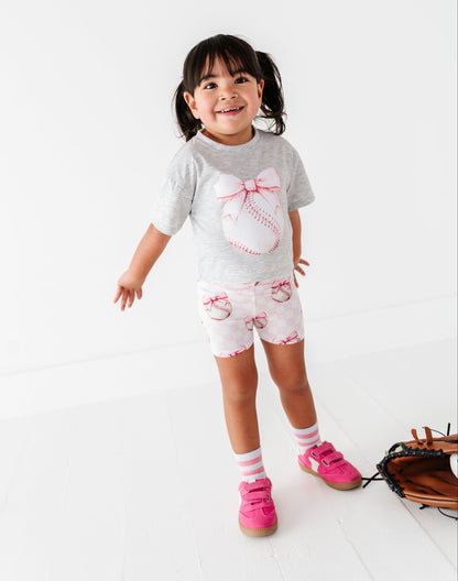 Little girl wearing a baseball-themed outfit featuring pink checkered bamboo shorts 
