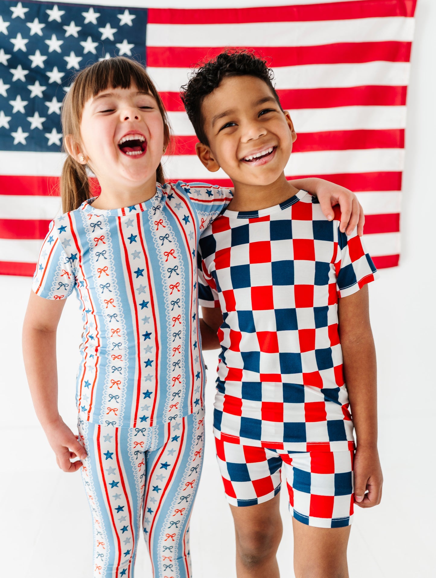 Two children wearing patriotic-themed bamboo outfits standing in front of an American flag.