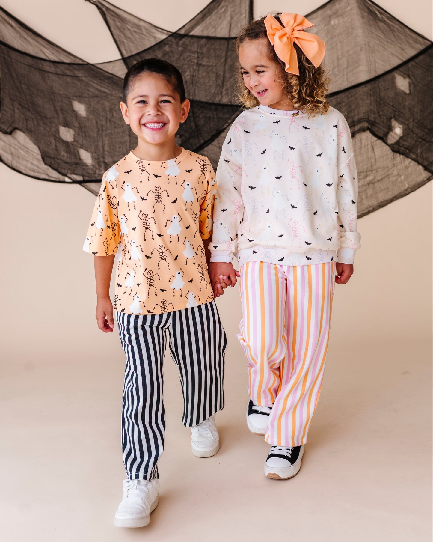 Two children holding hands in front of a decorative net, wearing patterned outfits.