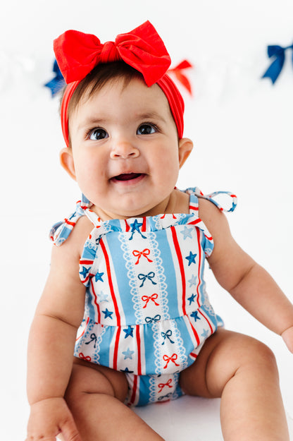 Baby wearing a red, white, and blue bamboo bubble romper with a bow on a white background