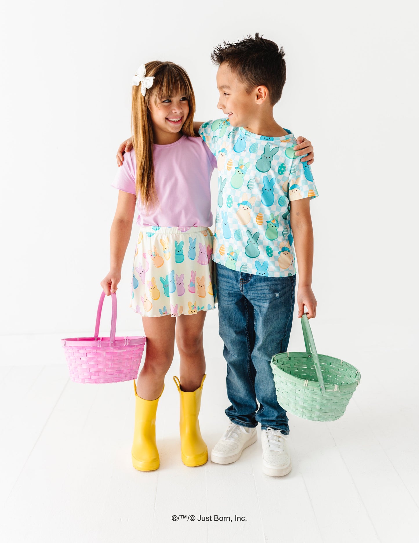 Two children standing together, one holding a pink basket and the other a green basket, on a white background.
