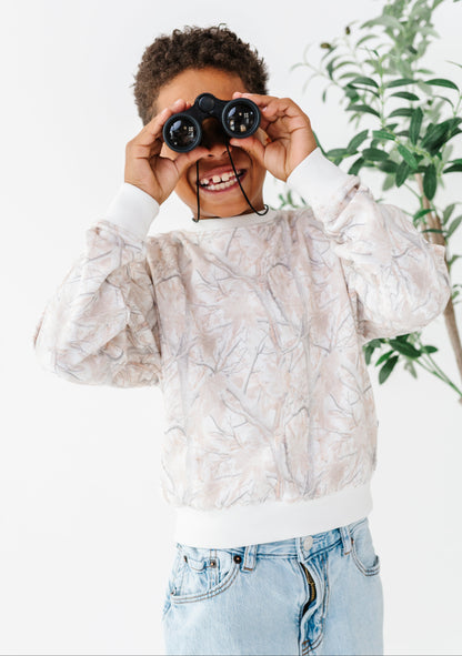 Child holding binoculars up to their eyes with a white background and plant in the corner