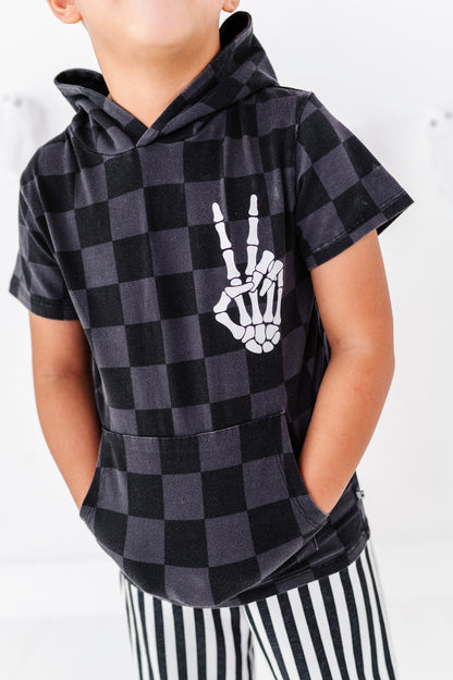 A child wearing a black and dark gray checkered hoodie with a white skeleton hand graphic on the chest, paired with black and white striped pants.