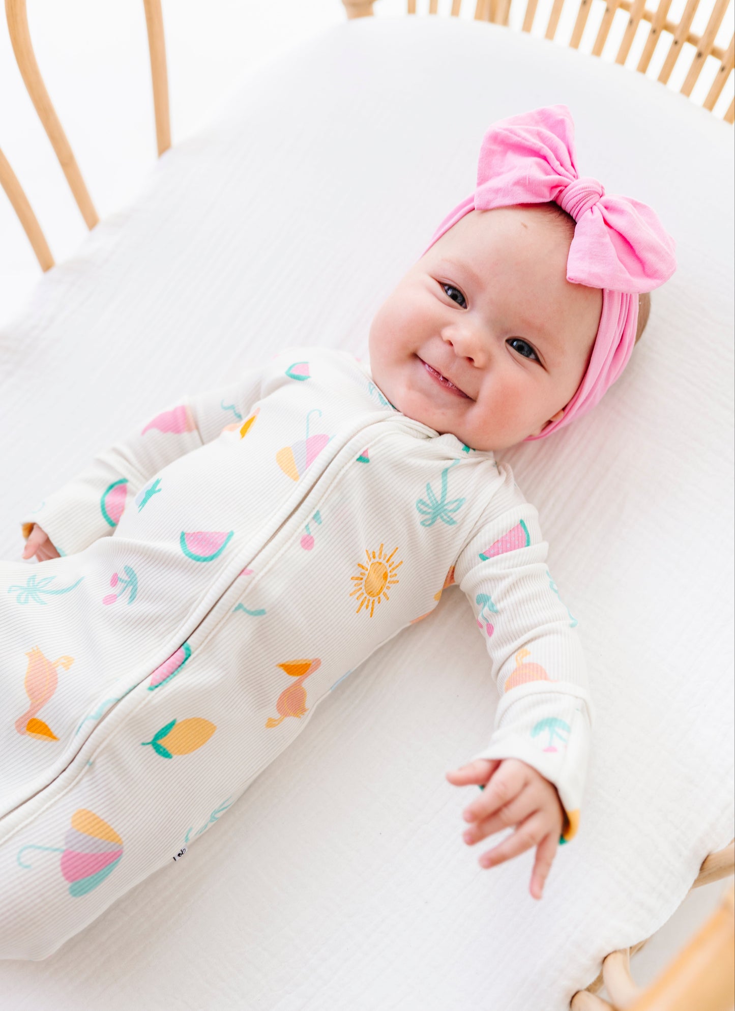 Baby in a colorful outfit with a pink headband lying on a white surface.
