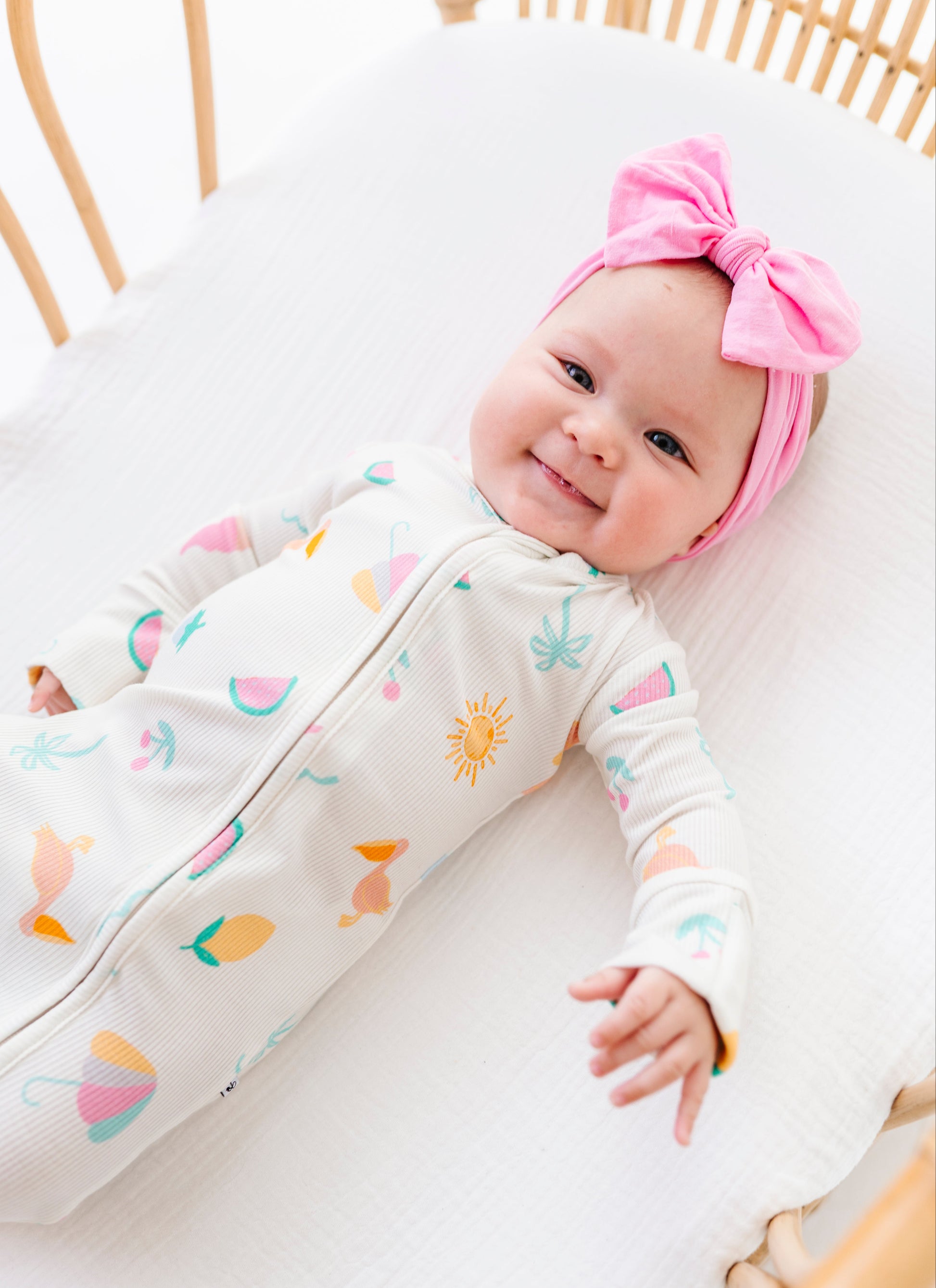 Baby in a colorful outfit with a pink headband lying on a white surface.