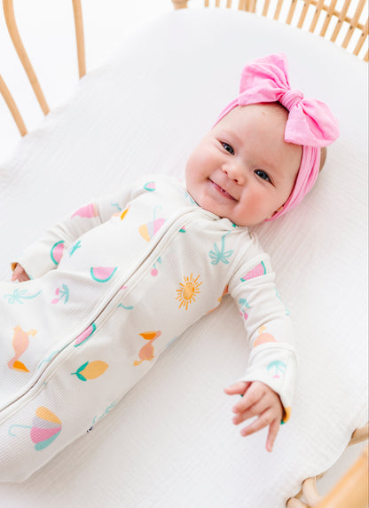 Baby in a colorful outfit with a pink headband lying on a white surface.