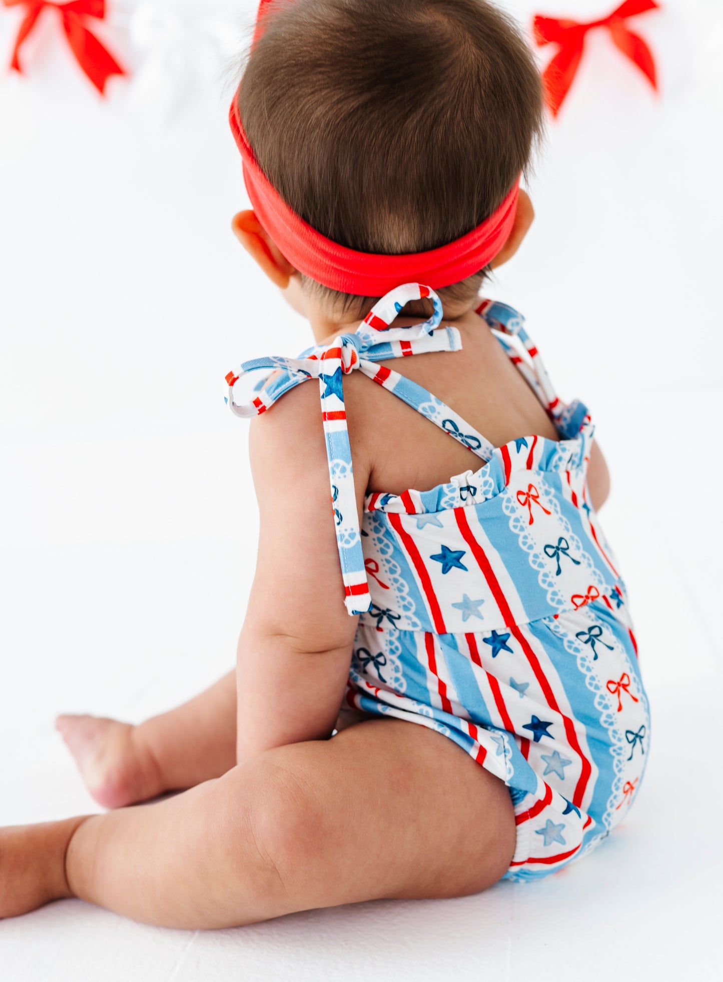 Baby wearing a red, white, and blue bamboo 4th of July-themed outfit with star pattern on a white background