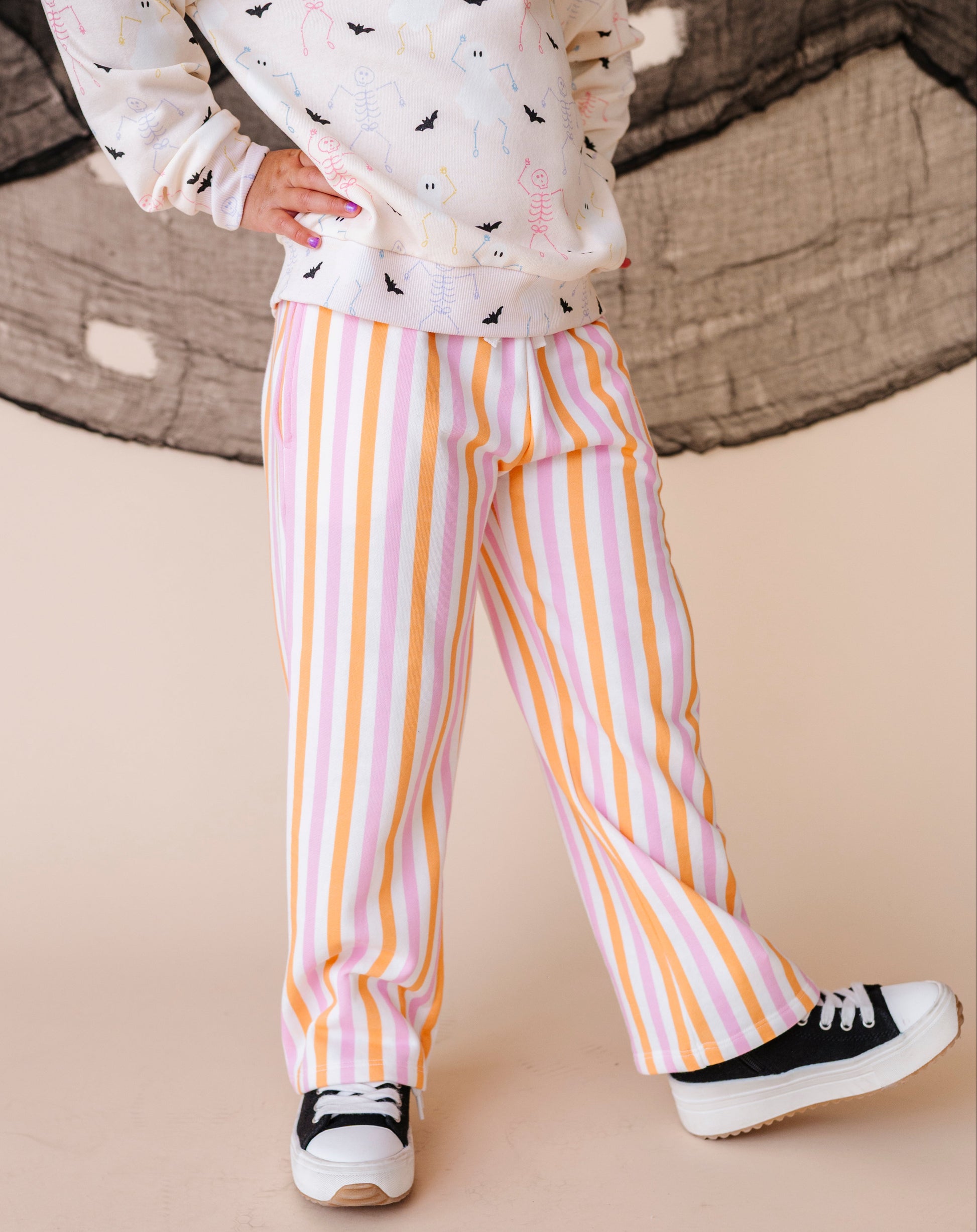 Child wearing a patterned sweatshirt and striped pants on a beige background