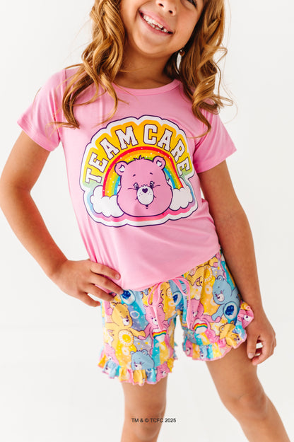 Child wearing pink Care Bears™ “Team Care” t-shirt with rainbow graphic and matching Care Bears print lounge shorts