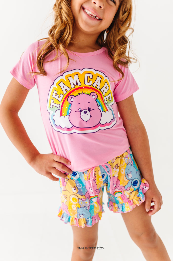 Child wearing pink Care Bears™ “Team Care” t-shirt with rainbow graphic and matching Care Bears print lounge shorts