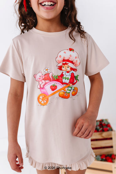 Child wearing a beige t-shirt set with a Strawberry Shortcake™ design on a white background