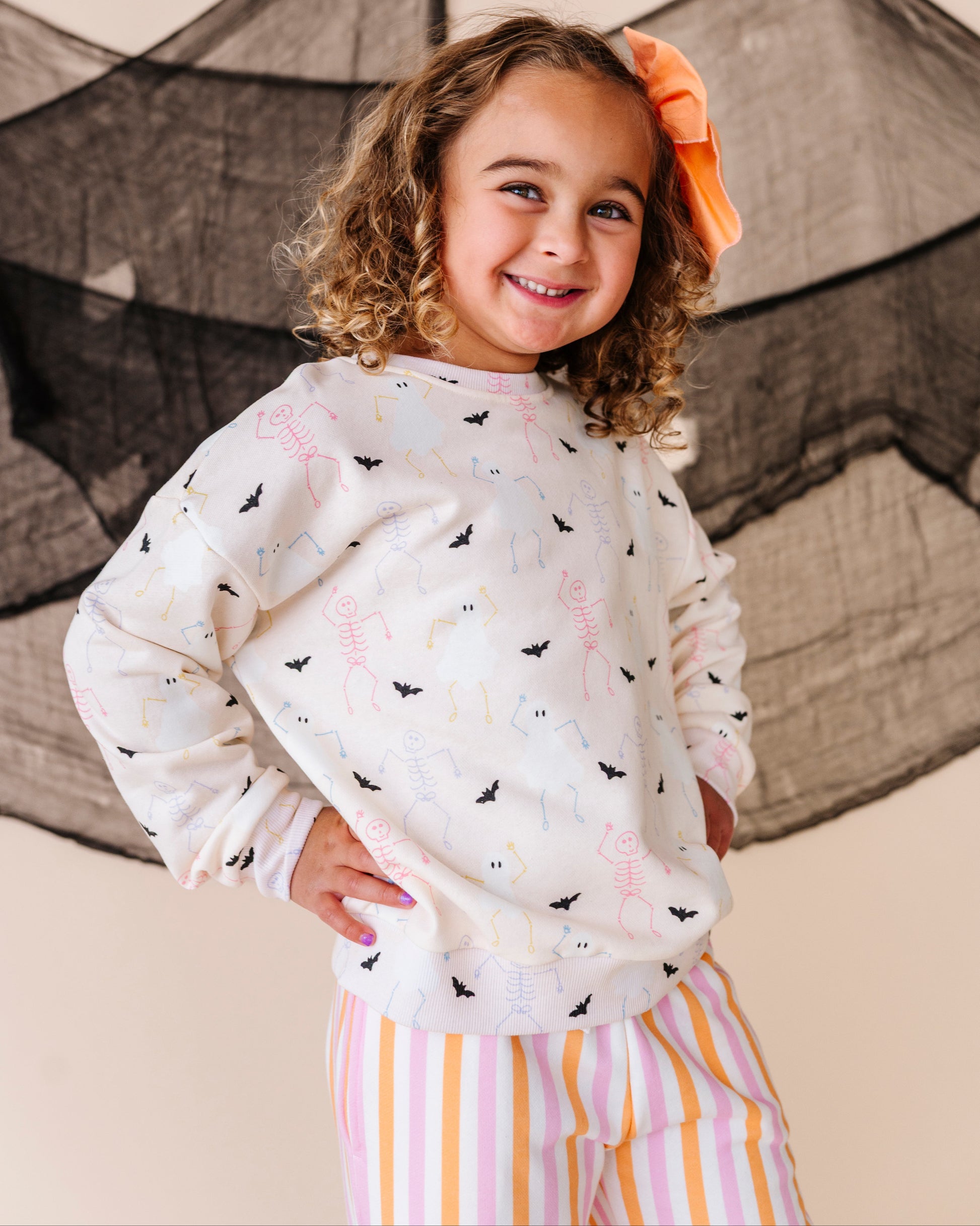 Child wearing a halloween patterned crewneck and striped pants with a large net in the background