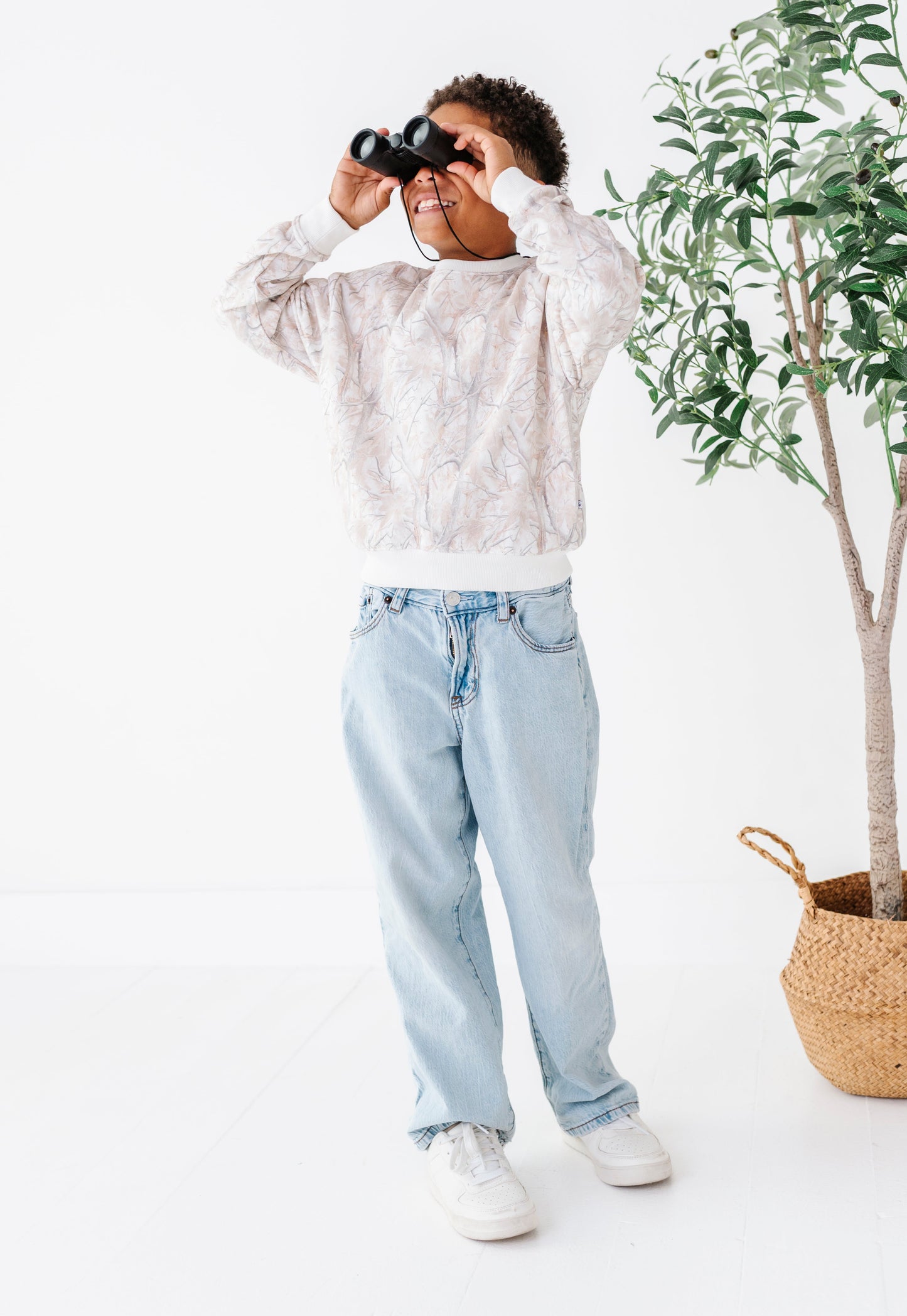 Person holding binoculars in a minimalistic setting with a plant and basket.