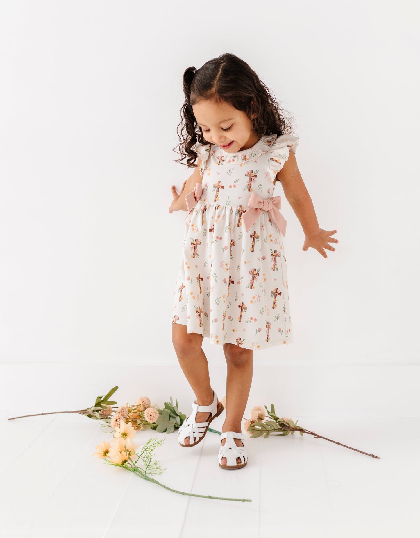 Young girl in a floral bamboo Easter dress standing on a white background with flowers around her.