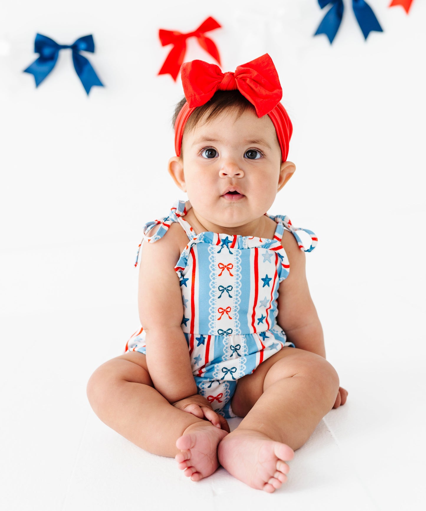 Baby wearing a patriotic outfit with red, white, and blue colors on a white background.