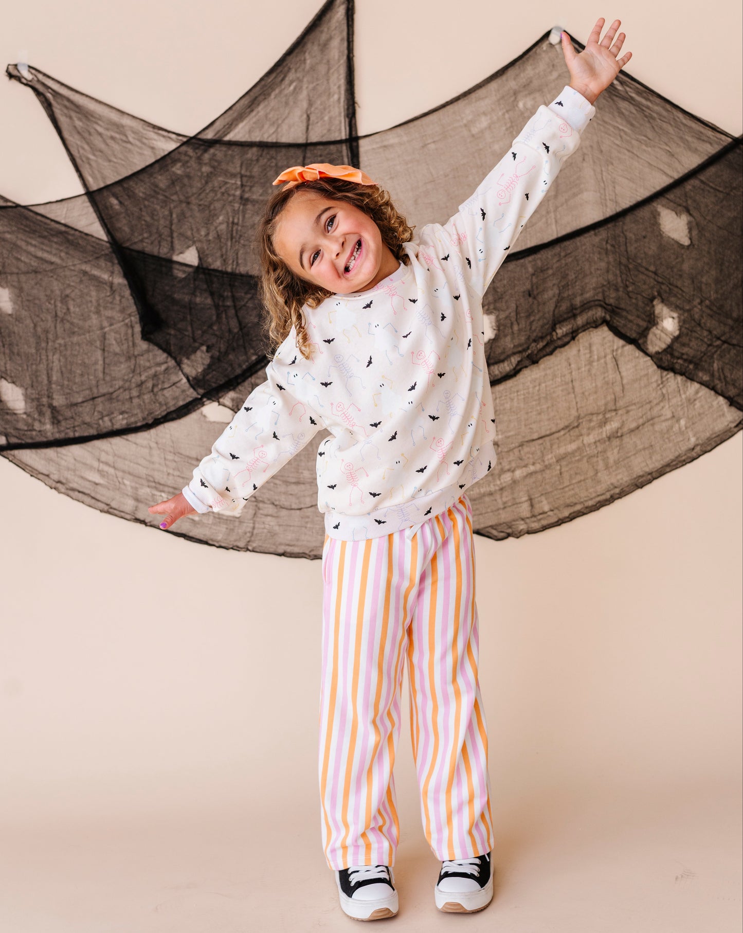 Child in a cream sweatshirt with halloween details and striped pants standing in front of a large net.
