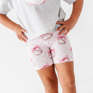 Child wearing pink checkered bamboo shorts with baseballs and bows 