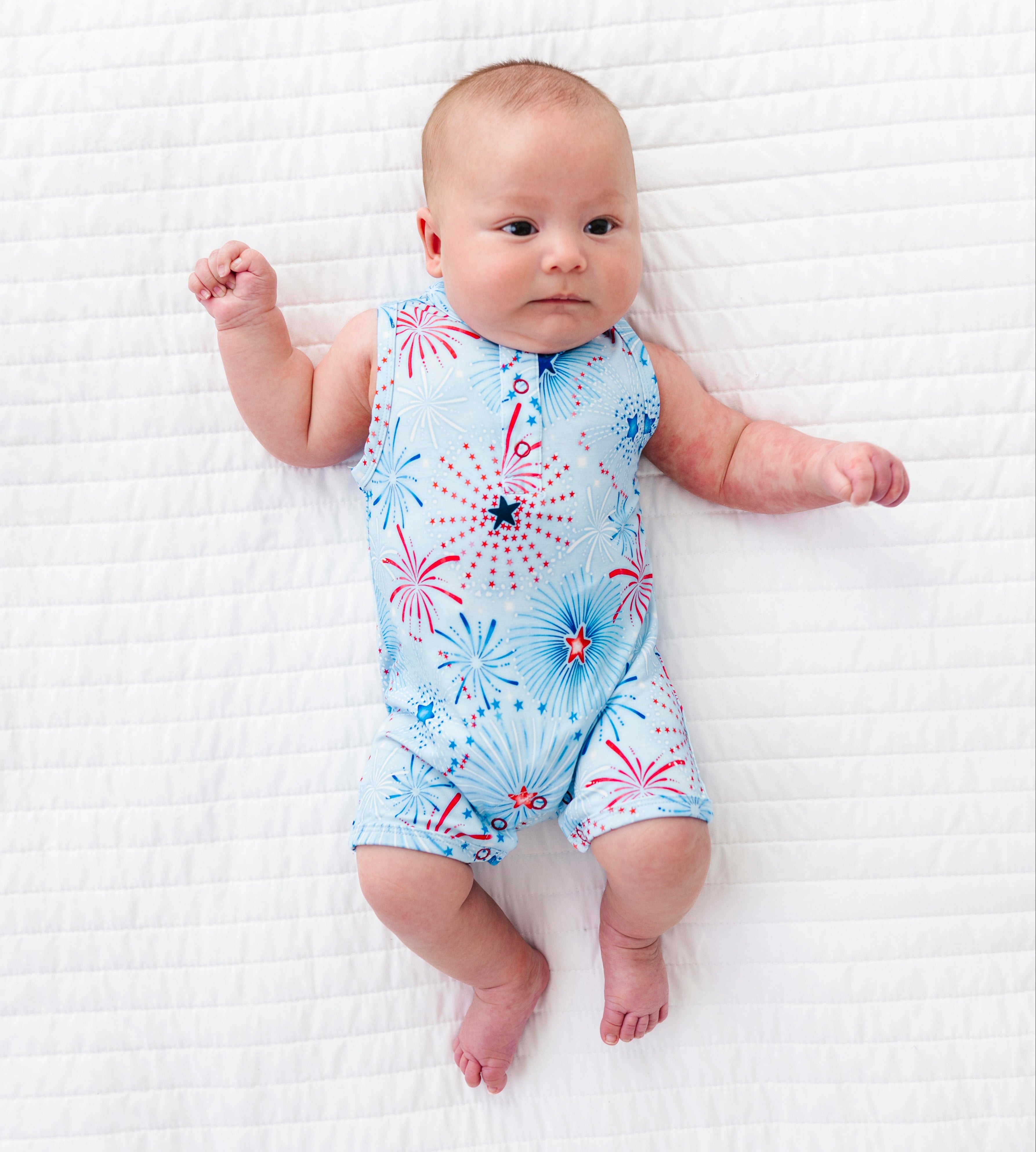 Baby wearing a colorful firework-patterned bamboo onesie on a white textured surface