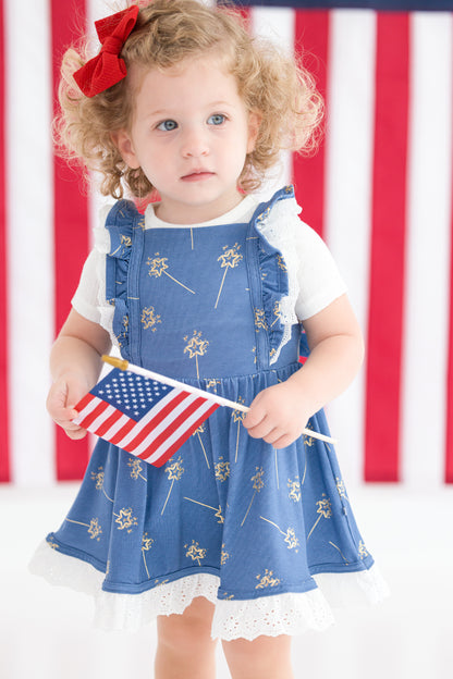 Child wearing a blue dress with white sparklers and holding an American flag in front of an American flag background