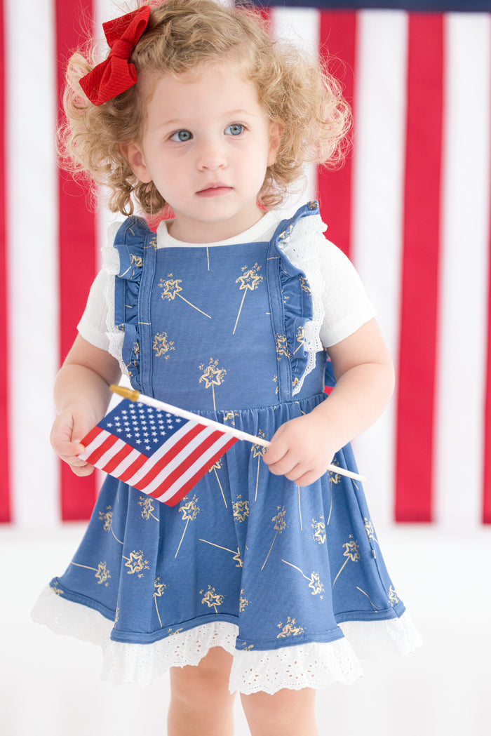 Child wearing a blue dress with white sparklers and holding an American flag in front of an American flag background