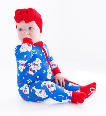 Child wearing Care Bears zip romper with red bow headband
