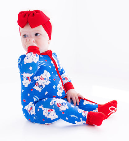 Child wearing Care Bears zip romper with red bow headband