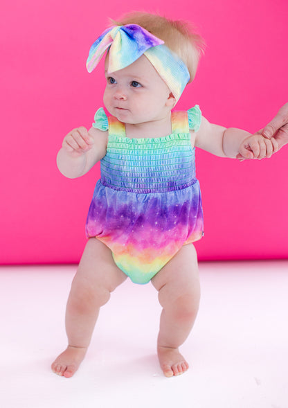 Baby wearing a colorful bow headband with a matching rainbow romper
