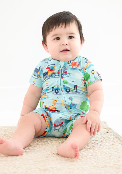 A baby sits, wearing a short-sleeve zip romper. The bamboo zip romper features animals driving trains, boats, cars, etc.