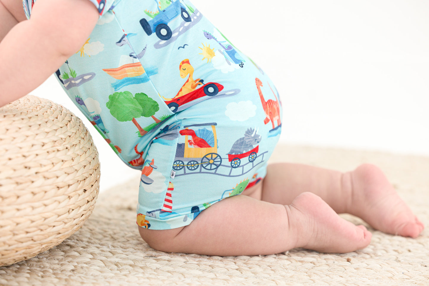 Baby wearing colorful patterned bamboo short zip romper with transportation design on a light blue background