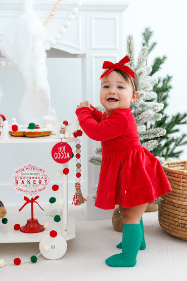 Baby in a red velvet dress with a matching velvet bow and green socks 