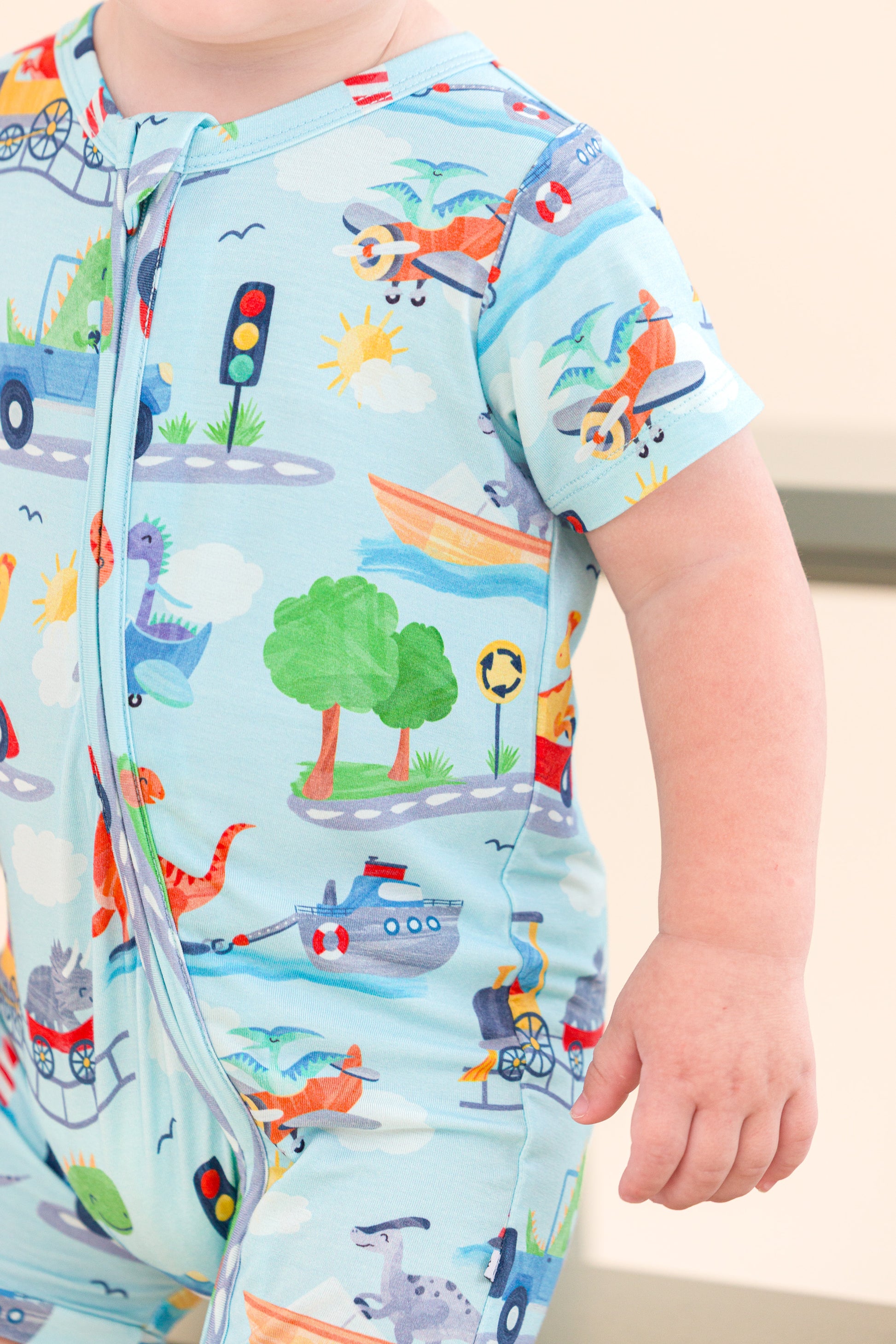 Child wearing a colorful bamboo onesie with vehicle and animal patterns on a light blue background.