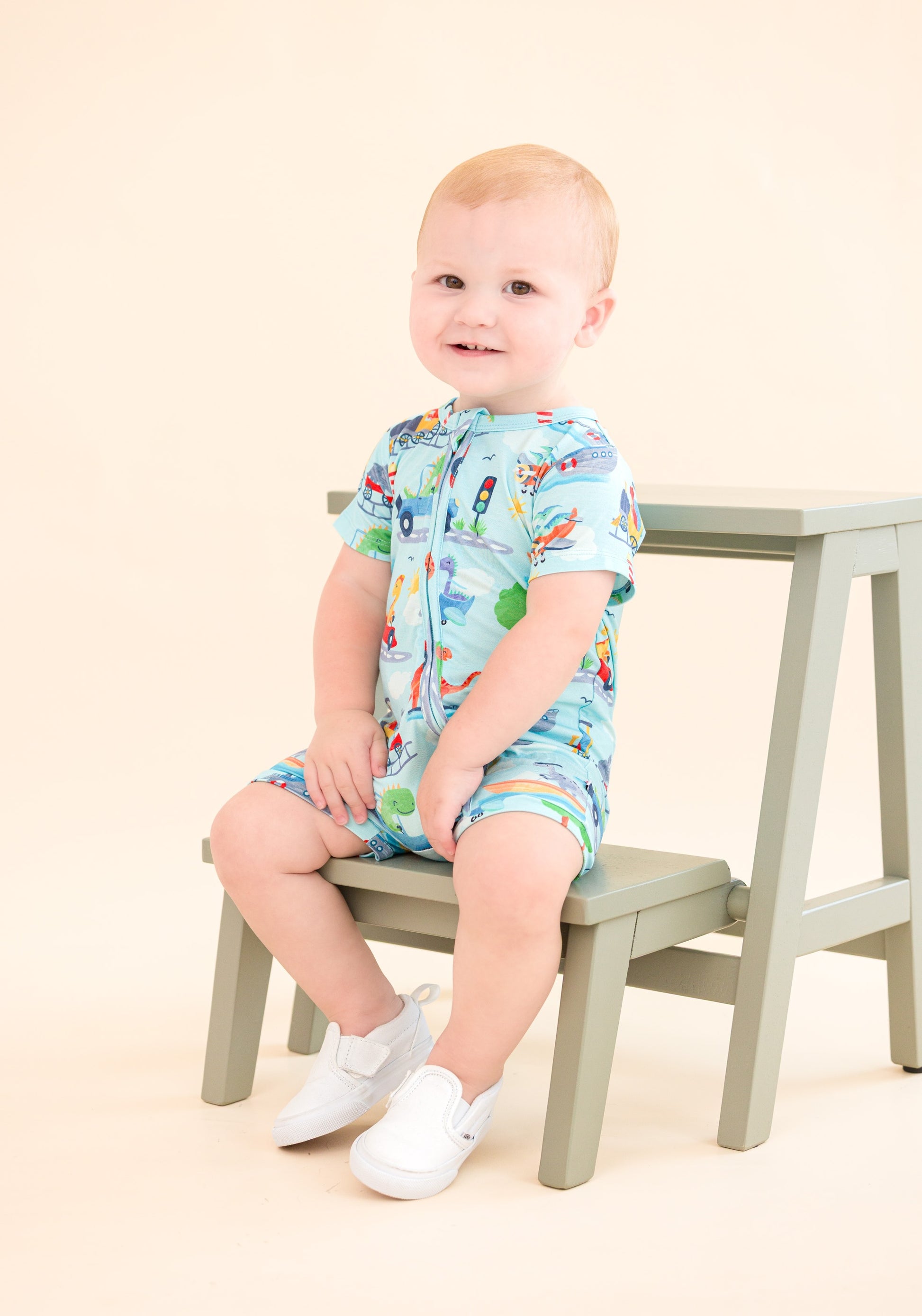 Baby sitting on a ladder wearing a colorful bamboo romper with vehicle pattern
