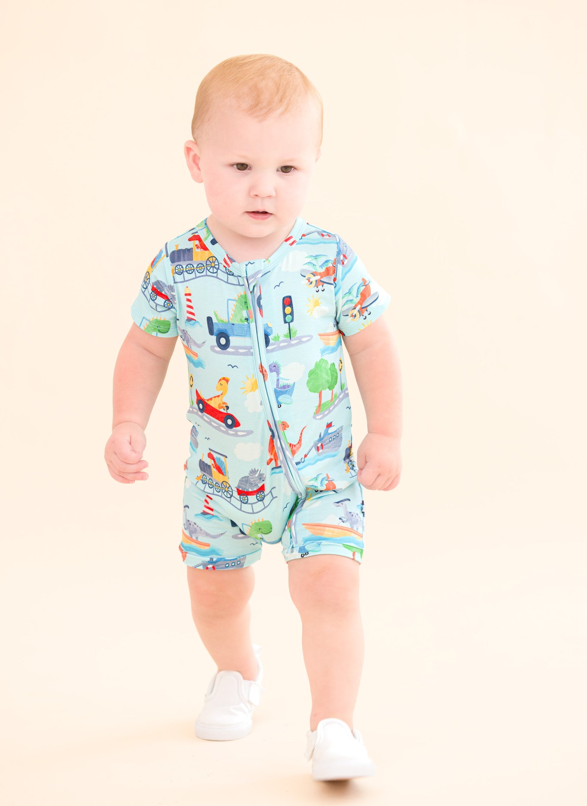 Baby wearing a colorful bamboo zip romper with vehicle prints on a beige background