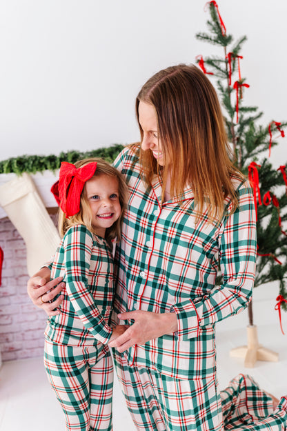 A mom and daughter standing in front of a Christmas tree wearing classic red-and-green plaid matching bamboo pajamas
