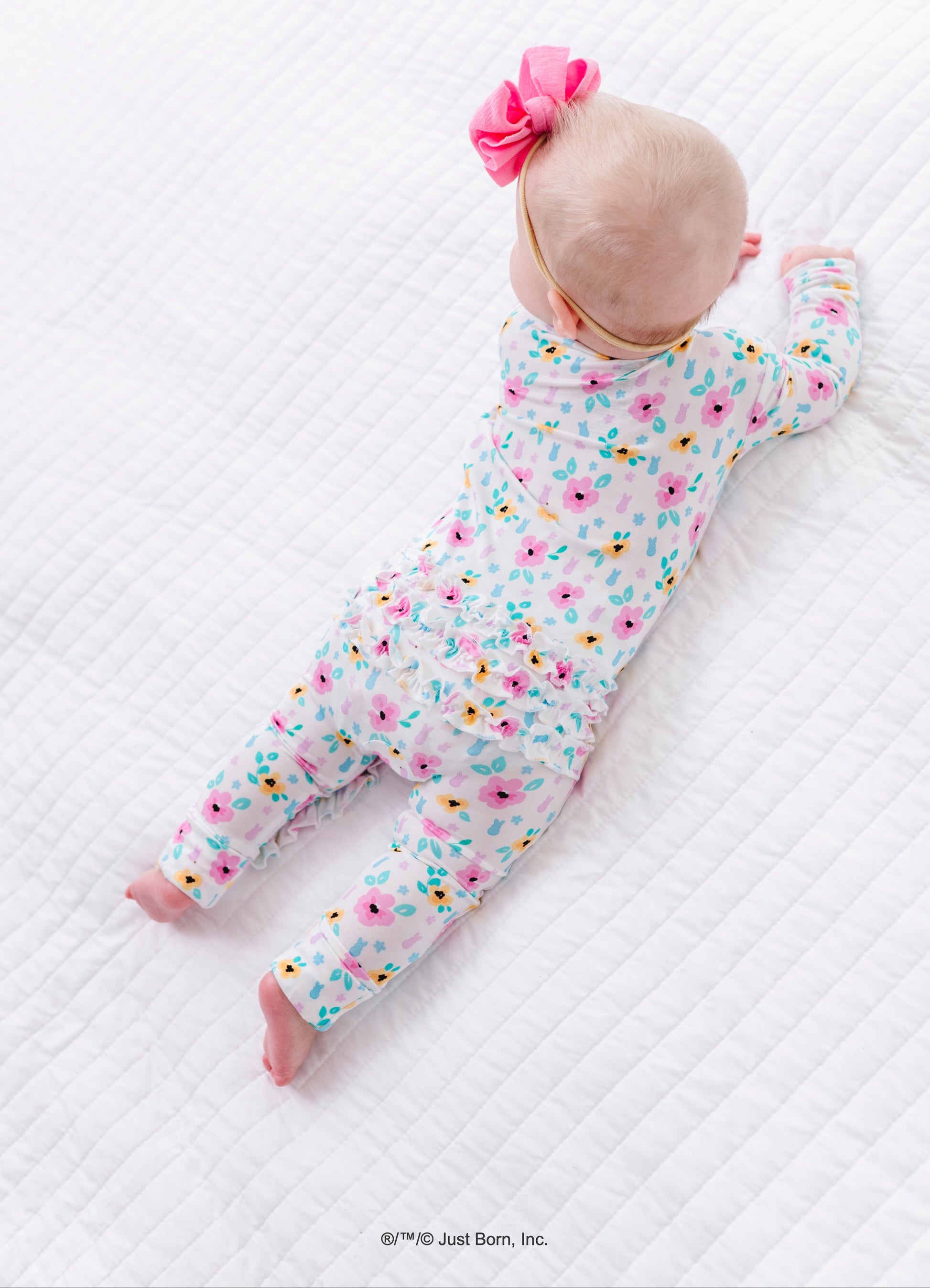 Baby in a floral PEEPS® bamboo onesie lying on a white textured surface