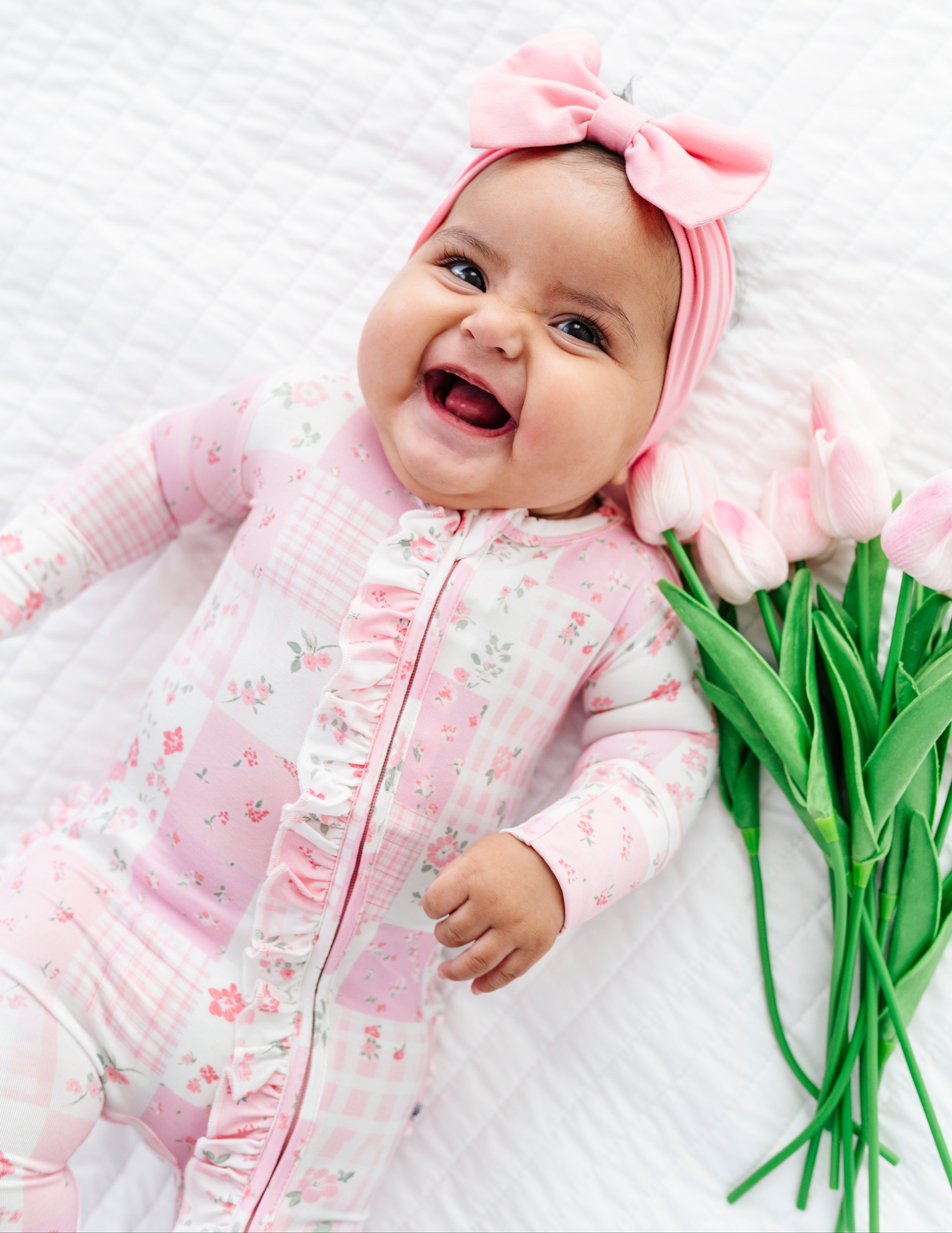 Baby in pink bamboo convertible romper with a pink bow, surrounded by pink tulips on a white background