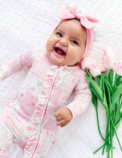 Baby in pink bamboo convertible romper with a pink bow, surrounded by pink tulips on a white background