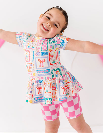 Child wearing a colorful sleeveless top and pink checkered shorts on a white background